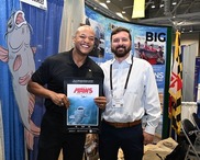 Two men holding at a booth promoting  fishing for blue catfish