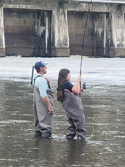 Girl working a fishing rod in a river near a large building