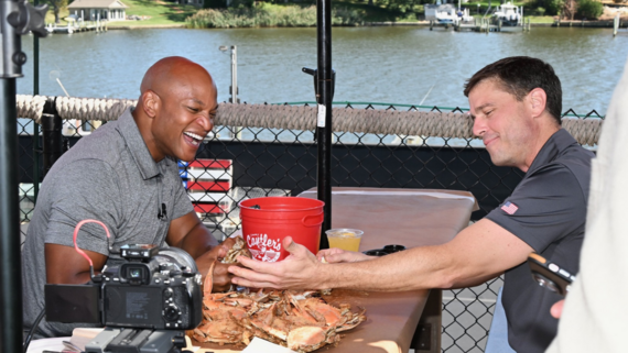 Governor Moore seated with Captain Reid Wiseman at a table with a tray of crabs