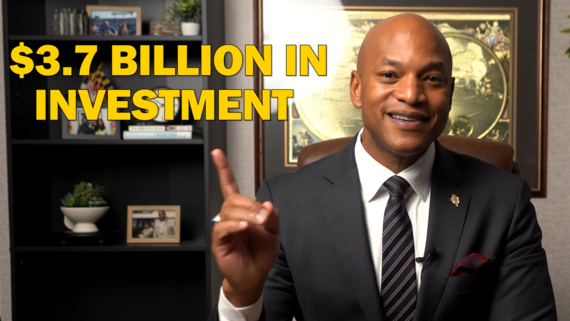 Governor Moore seated in office pointing to text on screen that reads "$3.7 Billion in Investment"