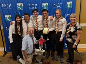 The Montgomery County Envirothon team pose with an award plaque in front of a blue NCF Envirothon backdrop, wearing matching Maryland ties. 