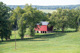 A red barn next to a brown fence surrounded by trees with a hillside and ridge of trees in the background, copyright Edwin Remsberg.,
