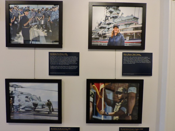 A wall display of four framed photos and plaques honoring women in the Navy, including Vice Admiral Yvette Davids and a helicopter on a flight deck.