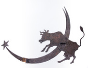 A weathered, rusted metal cutout of a horned cow jumping over a large crescent moon with a star at the tip.