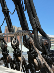 Close-up of intricate black and tan standing rigging, deadeyes, and wooden blocks on the USS Constellation ship.