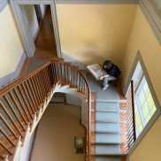 High-angle view of a person seated on a stair landing inside Riversdale House Museum drawing blueprints on a board.