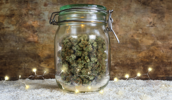 A jar of cannabis atop some snow with twinkle lights