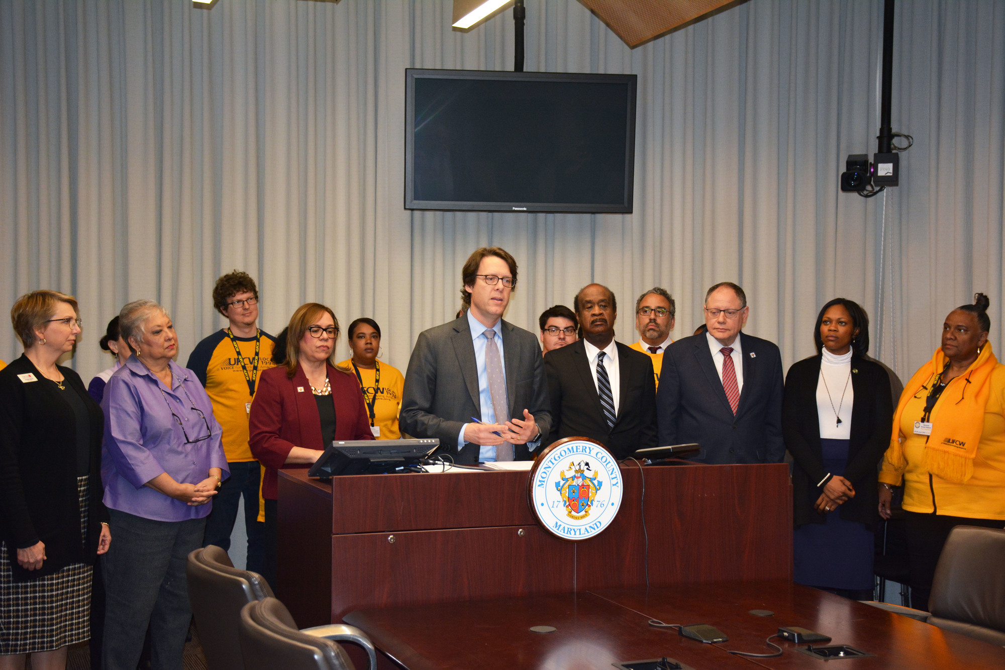 Council President Hans Riemer speaking with Councilmembers , County Executive, and County union representatives in the background