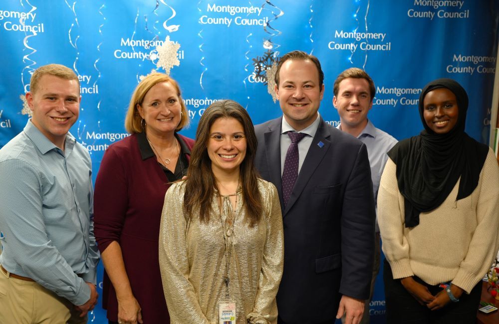 Team Friedson poses in front of a blue holiday backdrop with the Montgomery County Council logo.