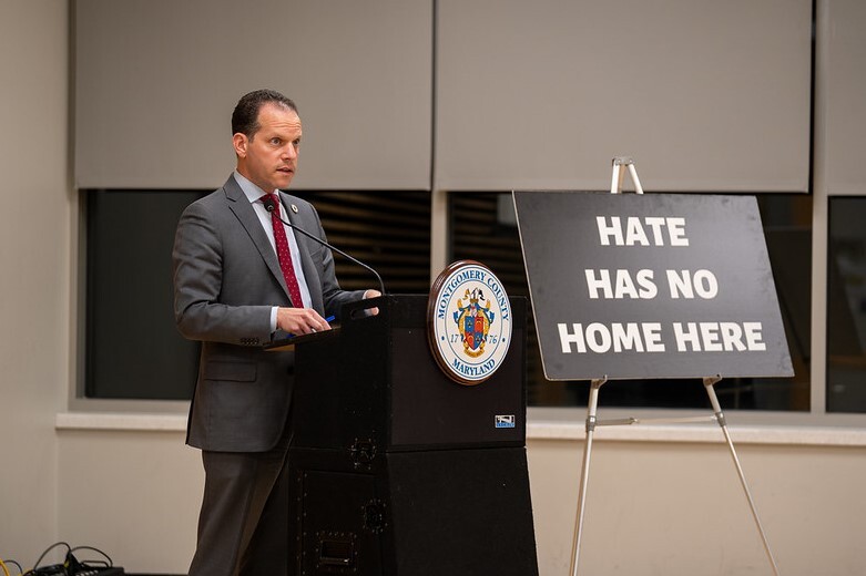 Councilmember Glass in front of a sign that says "Hate has no home here"
