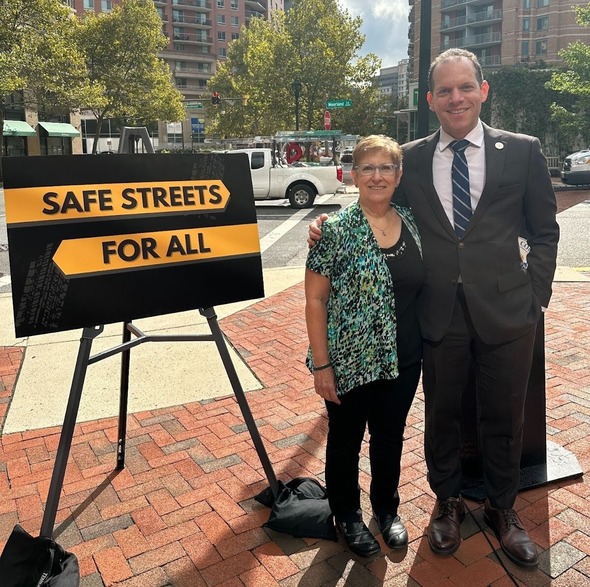 Councilmember Glass and a resident stand in front of a sign that reads "safe streets for all"
