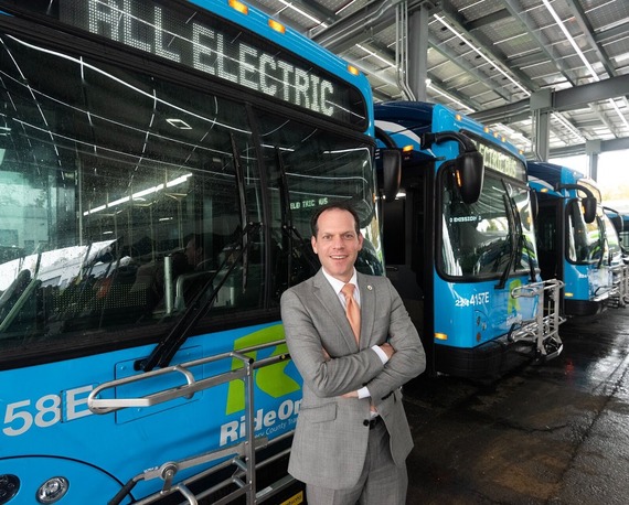 Councilmember Glass in front of a Ride On bus powered by electricity 