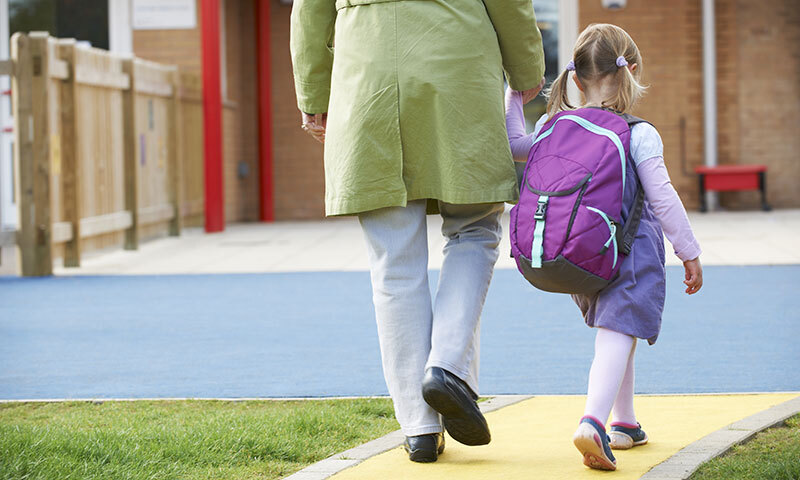 A child with a backpack walking to school while holding her mother's hand