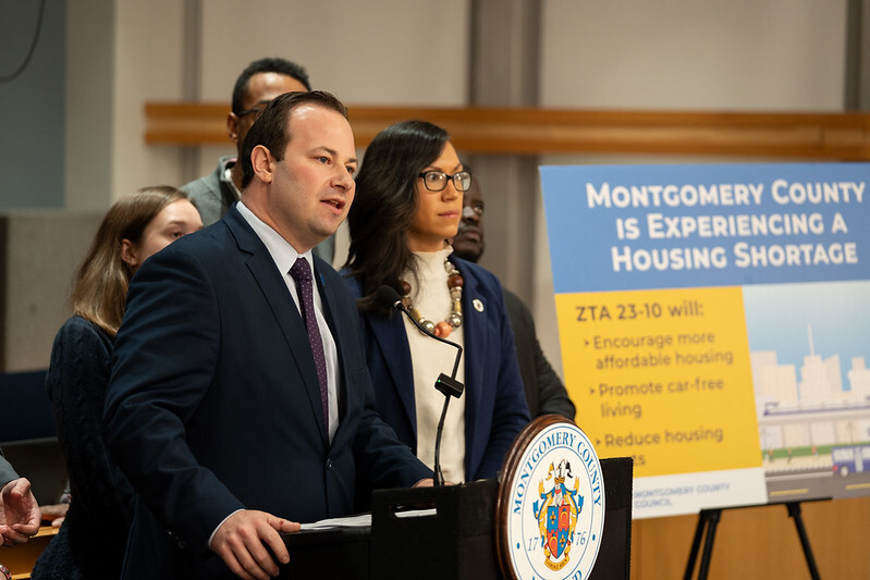 Council President Friedson speaks at a podium with Councilmember Mink. A poster board reads “Montgomery County is experiencing a housing shortage”.