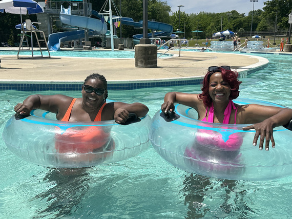 Two women smiling for a photo while riding inner tubes on a lazy river at the pool