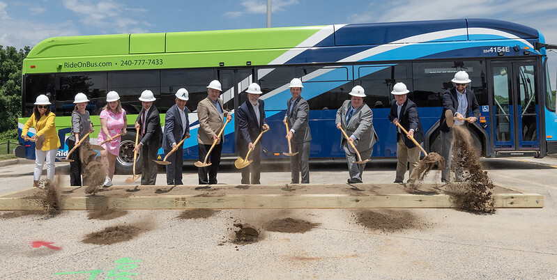 Elected officials and transportation leaders shovel dirt for the bus depot groundbreaking event in front of a Ride On bus.