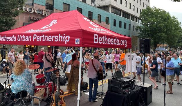 Musicians playing under a Bethesda Urban Partnership tent at a crowded outdoor concert.