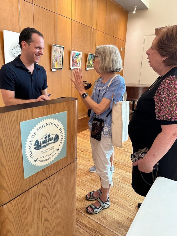 Councilmember Glass speaking with two residents in front of a podium bearing the official seal of the town of Friendship Heights