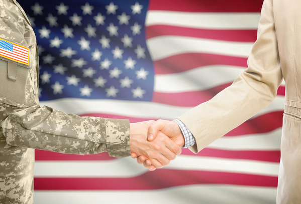 Service member shaking hands with a business person with the American flag as the backdrop.