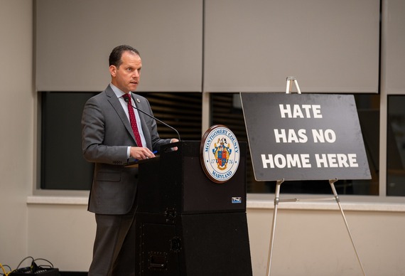 A photo of Councilmember Glass in front of a sign that says "Hate Has No Home Here"