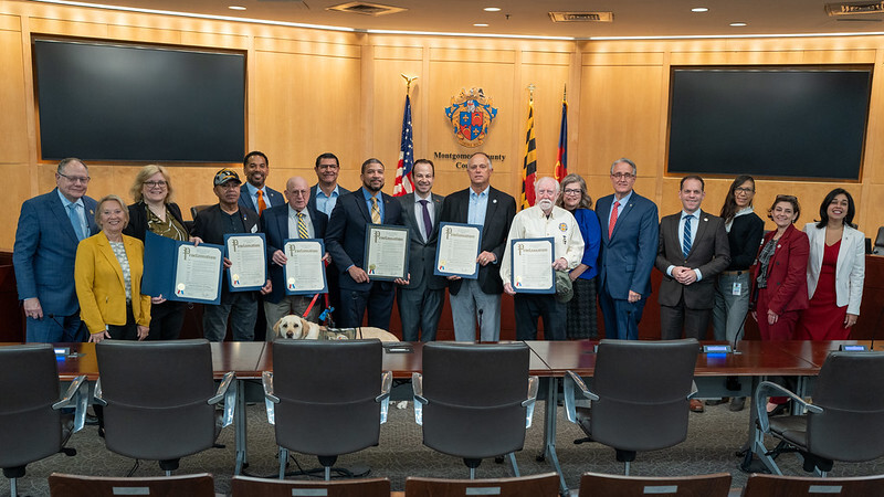 Councilmembers, veterans, community members and a service dog take a photo in the Council chamber.