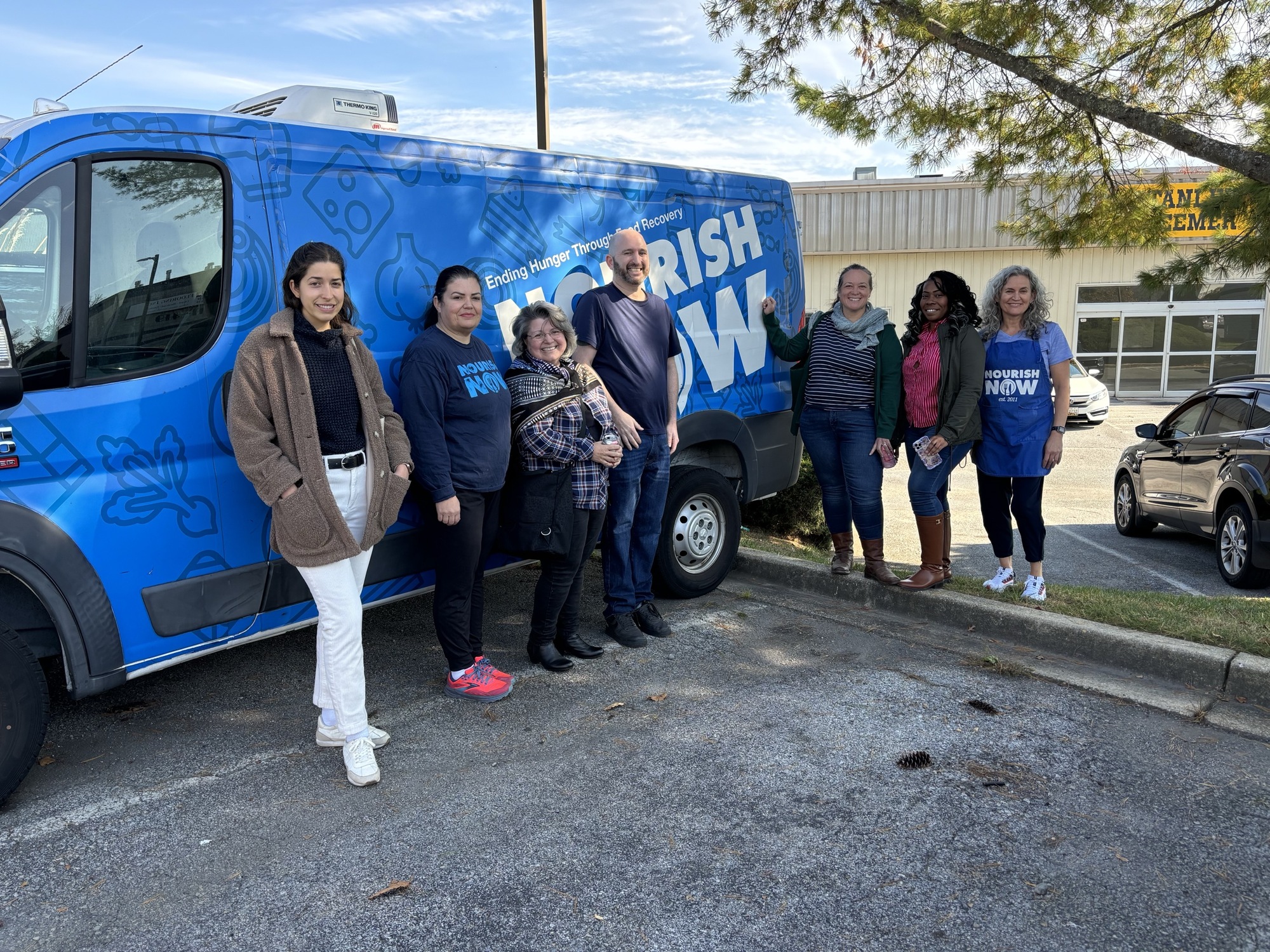 Group picture of OFSR staff with Nourish Now team in front of royal blue van with nourish now logo in large white letter on it