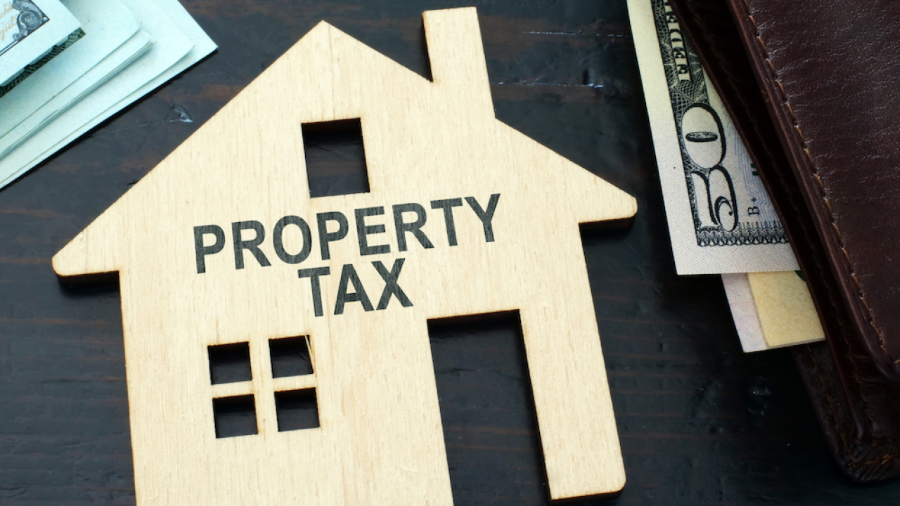 Small wood cutout of a house with the words “Property Tax” displayed. Credit: Canva.
