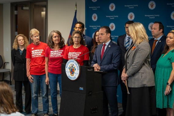Councilmember Glass speaks at a press conference next to three women in "Moms Demand Action" shirts