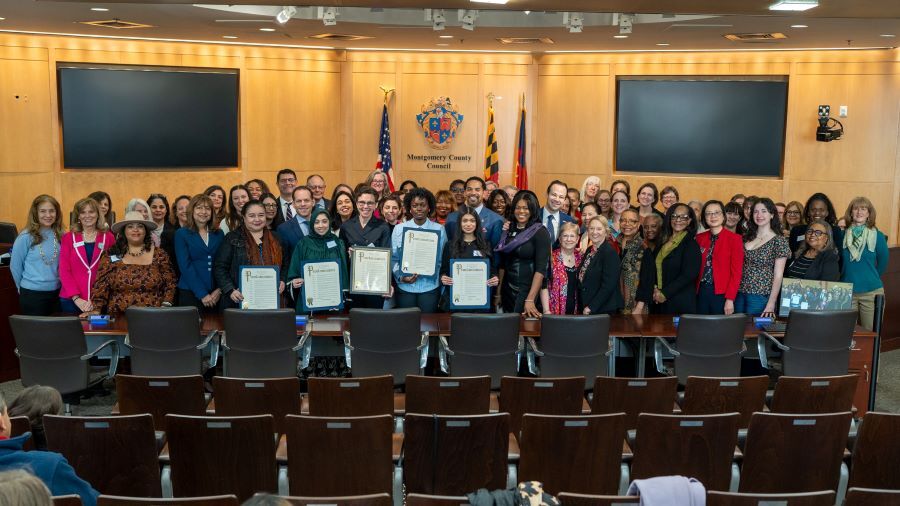 Large group shot of Councilmembers and women leaders in the Council chamber for a Women's History Month proclamation.
