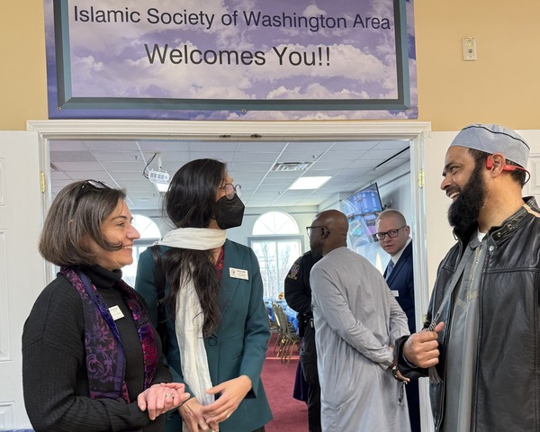 Councilmembers Stewart and Mink speak with community member under a sign "Islamic Society of Washington Area Welcomes You!!"