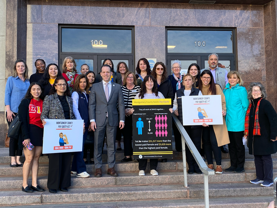 Councilmember Glass stands with a group of several people, mainly women, outside the Council Office Building holding signs about pay equity.