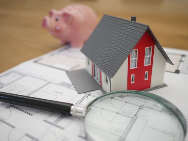 Model home with magnifying glass and piggy bank in the background.