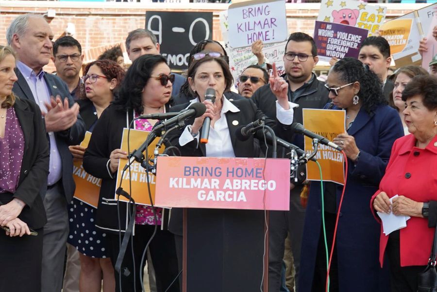 President Stewart speaks at a podium with a sign “Bring Home Kilmar Abrego Garcia” flanked by elected officials and supporters holding rally signs.