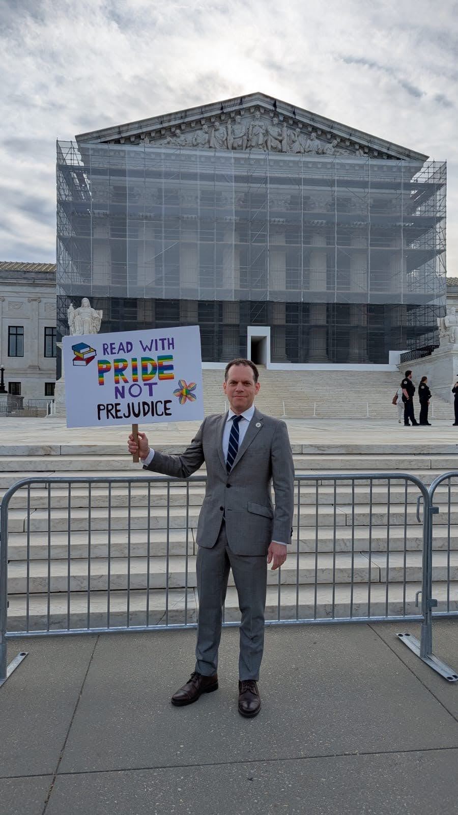 Councilmember Glass stands in front of the Supreme Court holding a sign that says "Read with Pride, not prejudice"