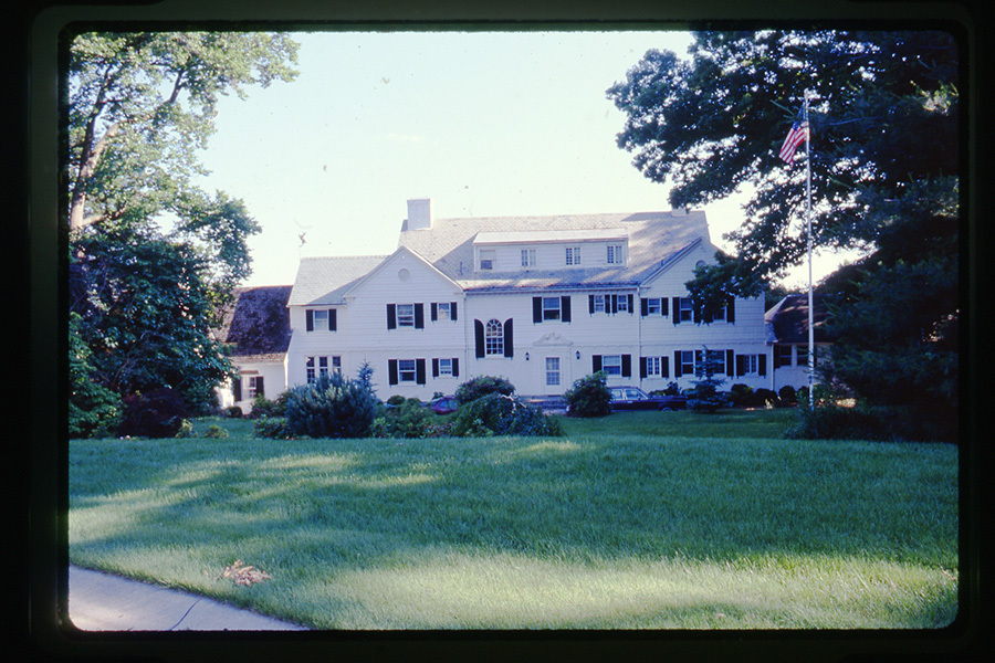 Historic Timberlawn. The large white house sits on a grass lawn with an American flag displayed on a flagpole.