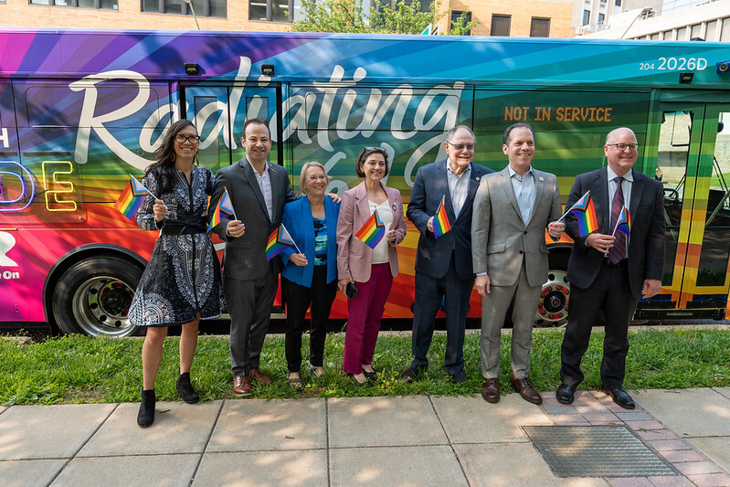 Councilmembers and Dept. of Transportation Director Conklin hold Pride flags and stand in front of the rainbow #RideWithPride Ride On bus.