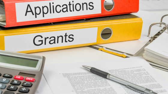 Two binders on a table. One binder has the word "applications" and the other binder has the word "grants." 