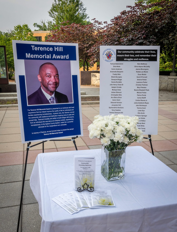 A poster listing the names of people who died while experiencing homelessness next to a poster with a photo and tribute to Terence Hill