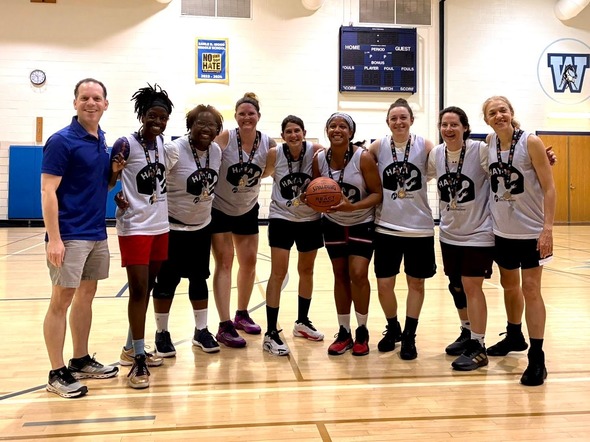 Councilmember Glass and eight women wearing Hoop As You Are jerseys stand on a basketball court. 