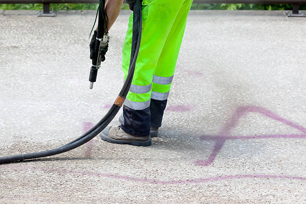 A worker covers graffiti with an airbrush and neutral-colored paint