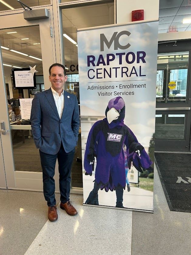 Councilmember Glass next to a poster of the Montgomery College Raptor mascot 