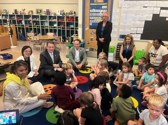 Mrs. Moore, Councilmember Glass, Superintendent Dr. Taylor, and other officials sit on a rug talking to a kindergarten class