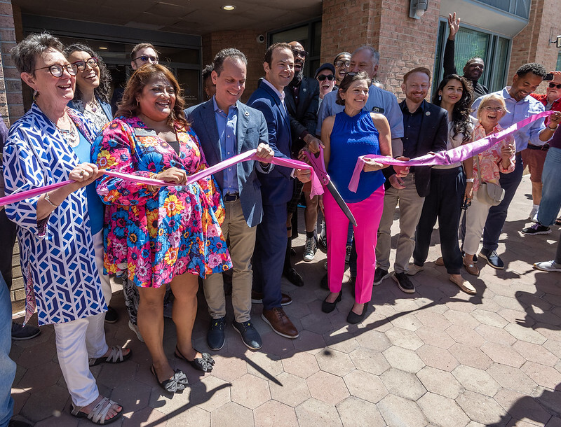 A group of elected and community leaders hold a pink ribbon at the MoCo Pride Center ribbon-cutting and grand opening.