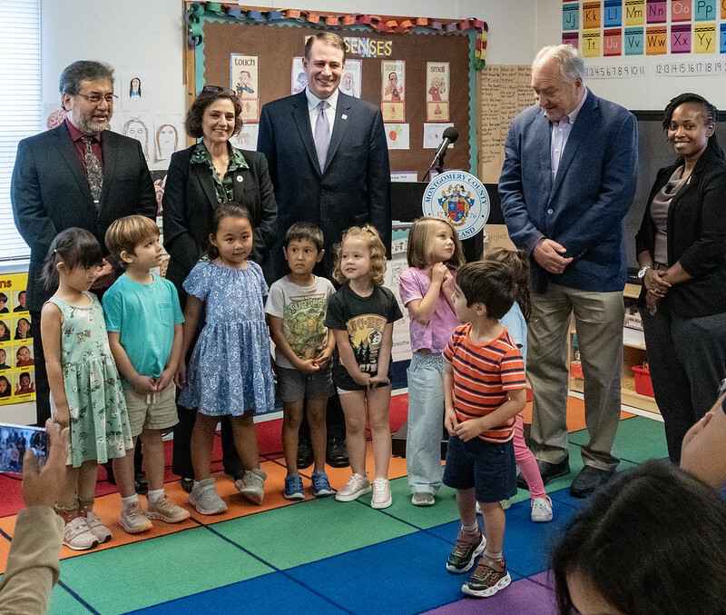 MCPS and County officials stand in a classroom with 8 early care students.