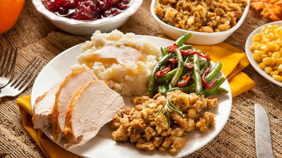 A traditional Thanksgiving meal featuring sliced turkey, mashed potatoes with gravy, stuffing, green beans, and cranberry sauce served on a plate.