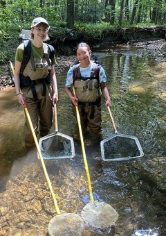 Two students are standing in a stream with monitoring equipment