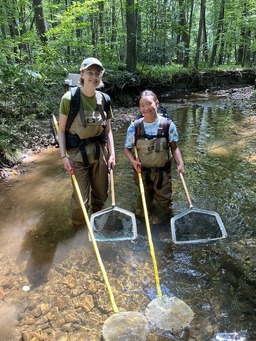 two female students standing in a stream with water quality monitoring equipment