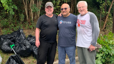 Three men standing near a stop sign smiling with full bags of trash near them