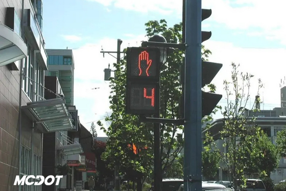 Photo of signal in downtown city with stores and trees in background. Has MCDOT logo.