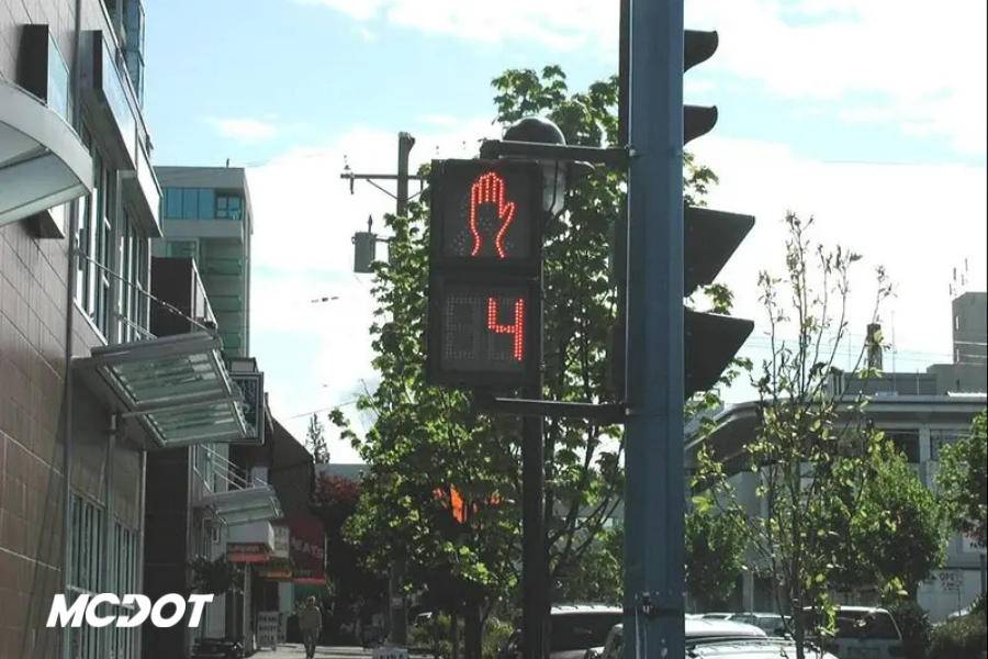 Photo of signal in downtown city with stores and trees in background. Has MCDOT logo.